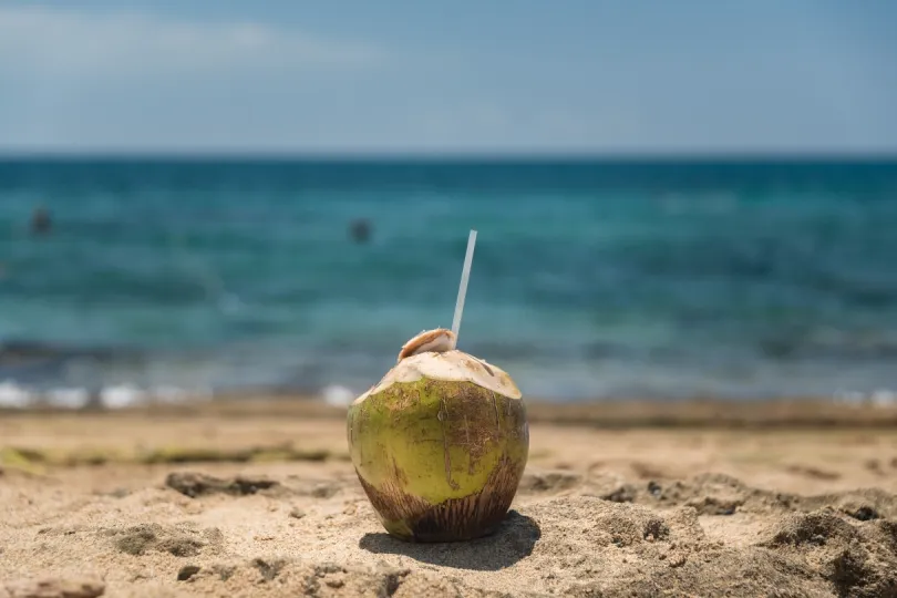Eine Kokosnuss mit Strohhalm am Strand