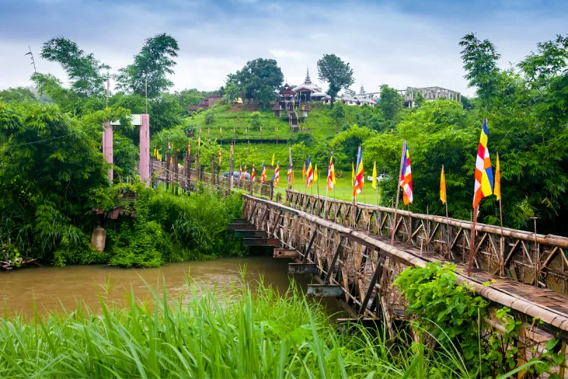 Eine Holzbrücke mit buten Fahnen führt durch die Reisfelder von Mae Hong Son