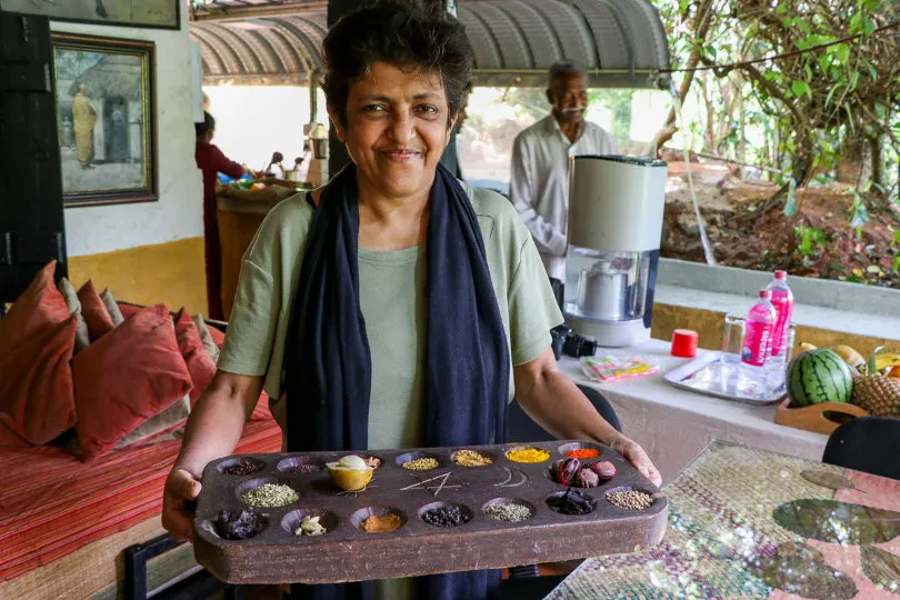 Eine Köchin steht in Sri Lanka mit einem Tablett und wartet auf die Teilnehmenden des Kochkurses