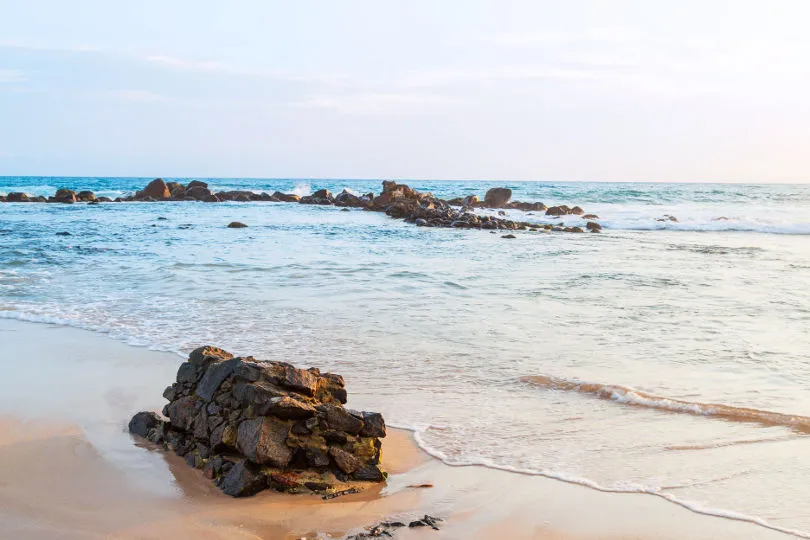 Ein Stein liegt auf dem ansonsten leeren und sandweißen Strand Sri Lankas