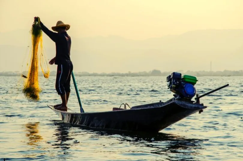 Ein burmesischer fischer sitzt auf einem boot und hält ein handgefertigtes  netz im inle-see, myanmar