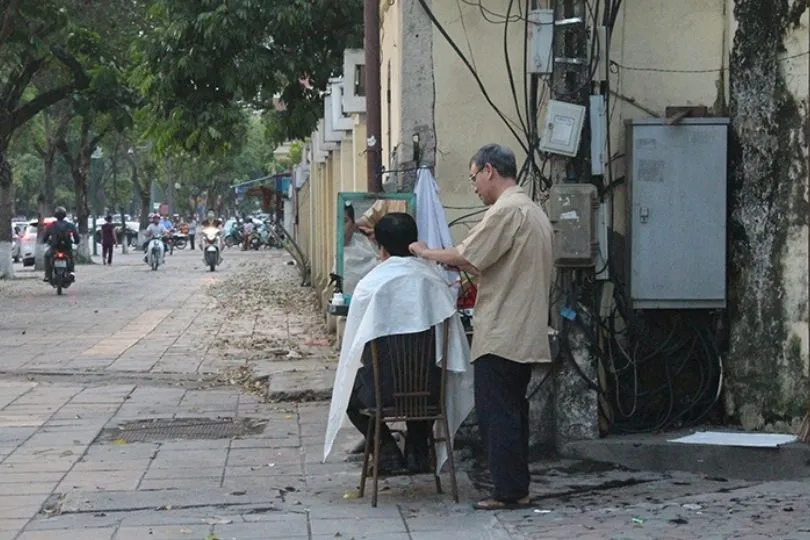 Normale Straßenszene in Hanoi: Friseure schneiden Haare