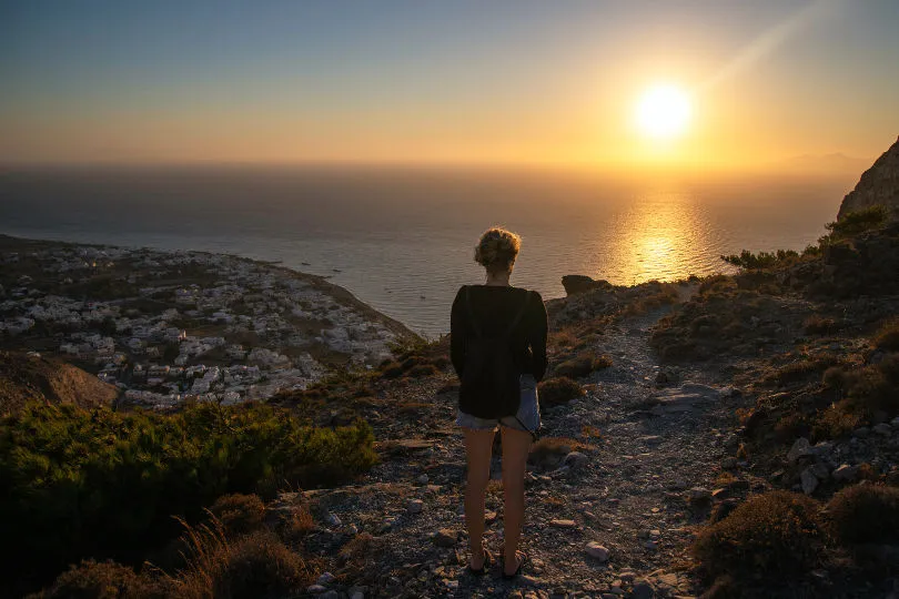 Eine Frau steht an einer Klippe in Griechenland und schaut auf das Meer