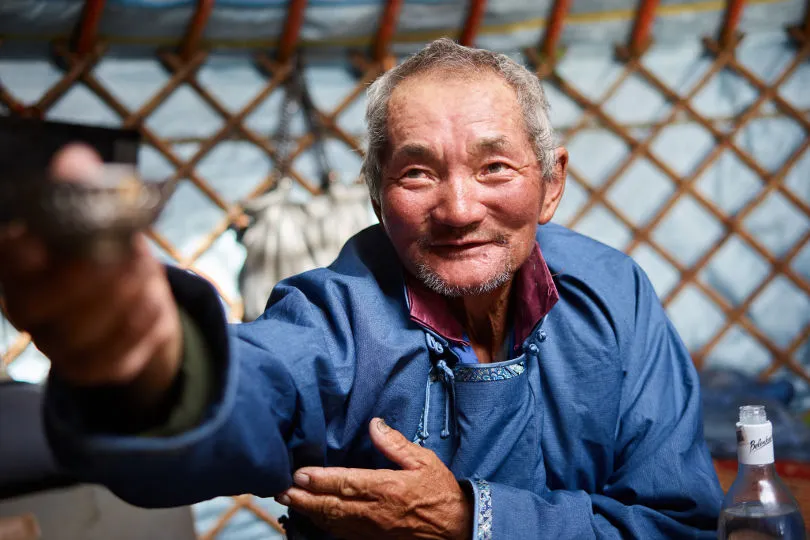 Ein Mann in der einer Jurte in der Mongolei hält eine Schale in die Kamera