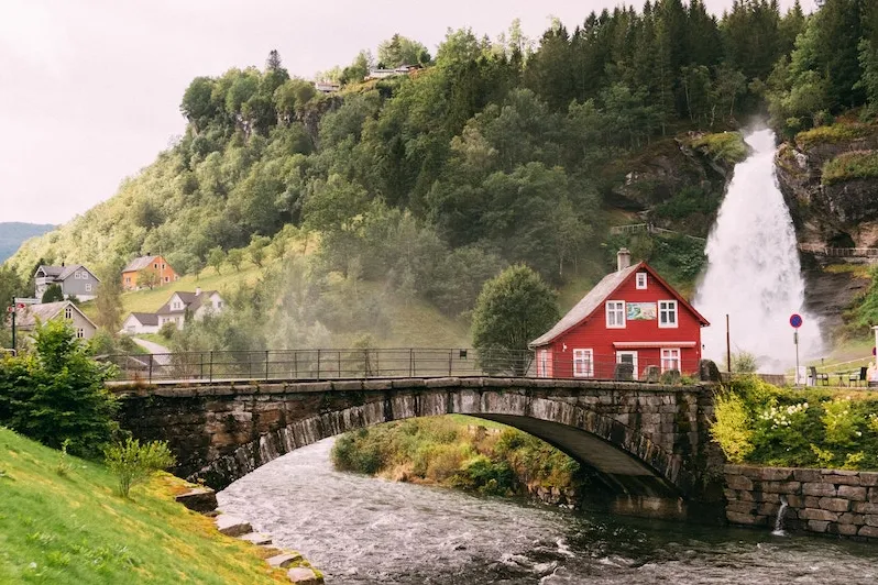 Rotes Häuschen bei einer Brücke und einem Wasserfall in Steinsdallsfossen, Norwegen.