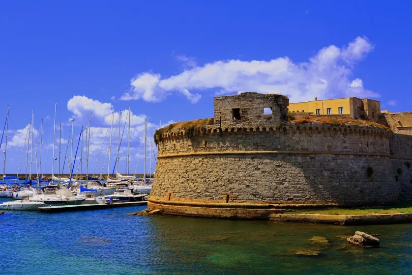 Schloss in Salento am Wasser mit mehreren Segelbooten.