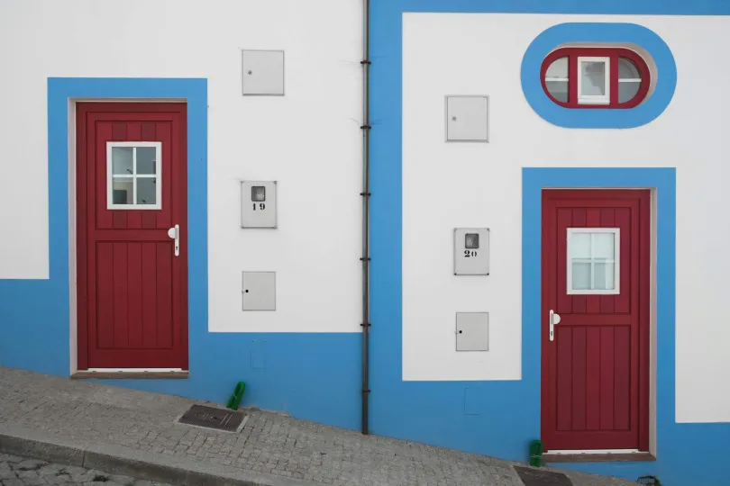 Zwei Häuser in Odeceixe mit roten Türen und blauen Verzierungen.