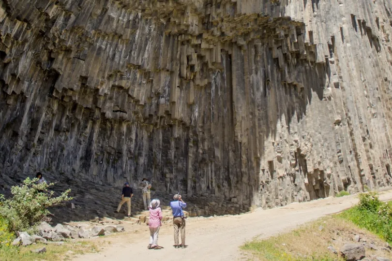 Paar Menschen stehen vor einer beeindruckenden Felsformation, die aus senkrechten Basaltsäulen.