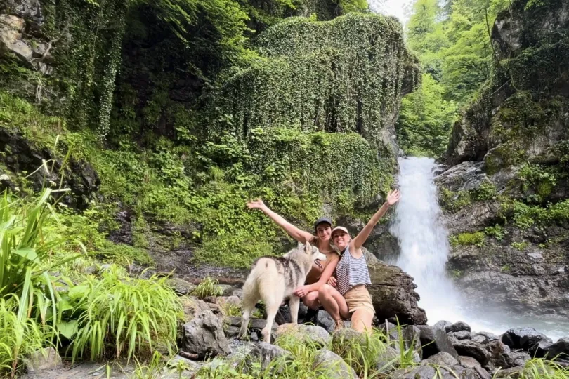 Zwei personen sitzen vor ein Wasserfall mit ein Hund.