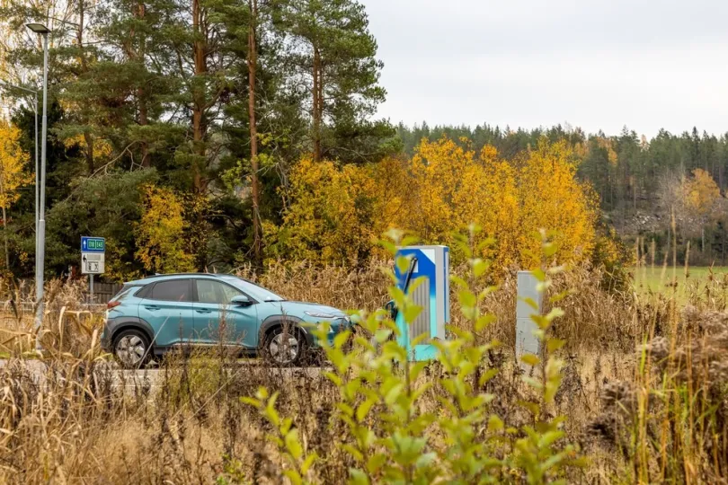 Elektroauto wird an einer Ladestation in einer natürlichen Umgebung mit Herbstfarben in Schweden aufgeladen.