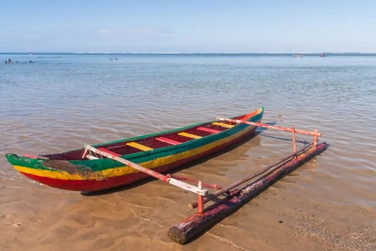 buntes Auslegerkanu aus Holz am Sandstrand mit flachem Wasser.