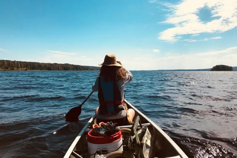 Ein Person mit Hut und Schwimmweste, die in einem Kanu ist und paddelt.