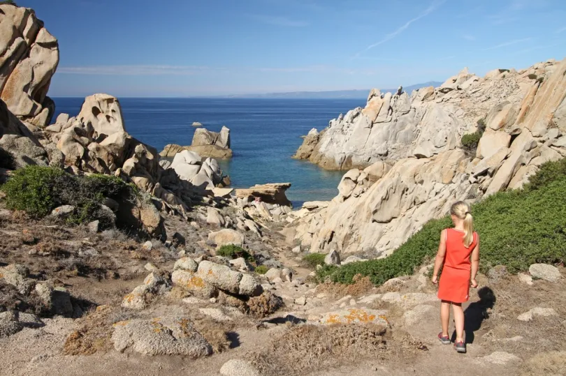 Ein Kind im orangefarbenen Kleid, die über Felsen zum Meer geht.