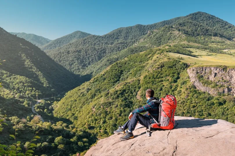 Mann mit Trekkingrucksack, der auf einer Klippe in den armenischen Bergen sitzt