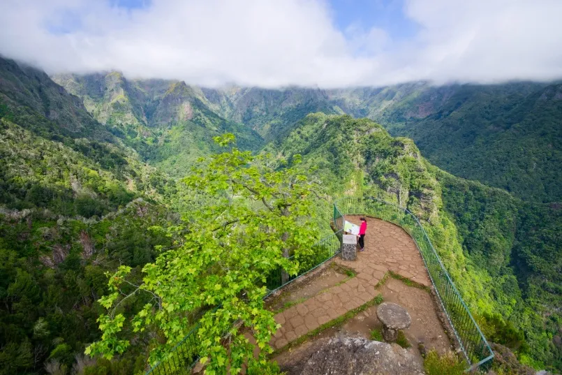 Ein Blick von oben auf die Vereda dos Balcões – eine Frau steht am Aussichtspunkt und orientiert sich, umgeben von sattgrüner Natur und dem weiten Panorama der madeirensischen Berge.