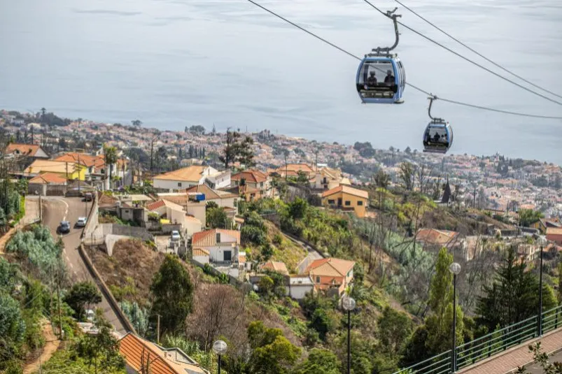 Blick auf die Stadt Funchal auf Madeira, über der sich eine Seilbahn elegant durch die Luft zieht.