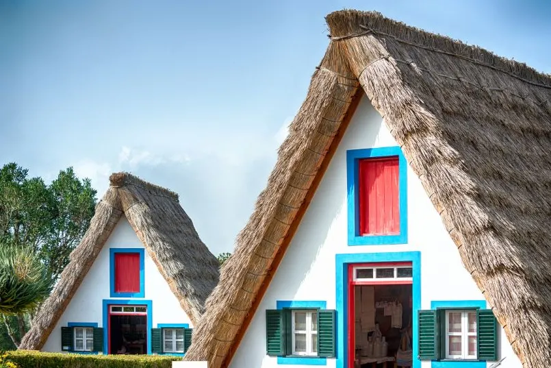 Ein traditionelles Quinta-Häuschen mit roten Akzenten, vor dem ein Baum steht – charmant eingebettet in die Landschaft Madeiras.