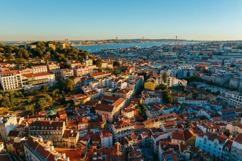 Blick von oben auf die Hauptstadt Portugals, Lissabon, mit vielen Häusern und einem Fluss im Hintergrund.