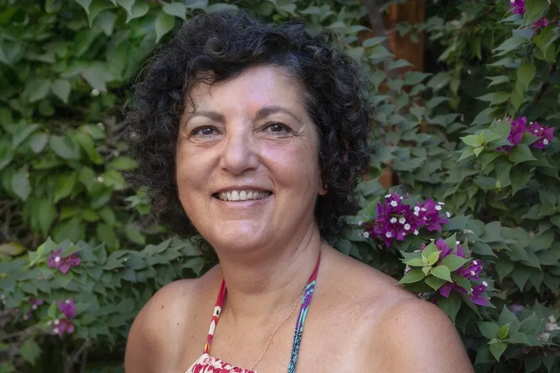 Portraitfoto einer Frau mit dunklen Locken vor begrünter Fassade.