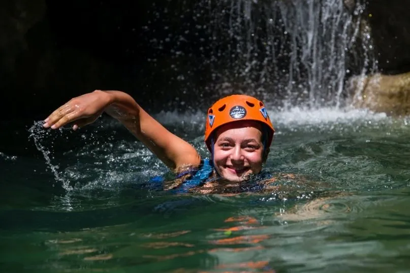 Eine Frau, die lächelnd mit einem Helm auf dem Kopf schwimmt.