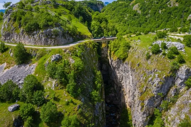 Ein Auto fährt in der Ferne zwischen den grünen Bergen.