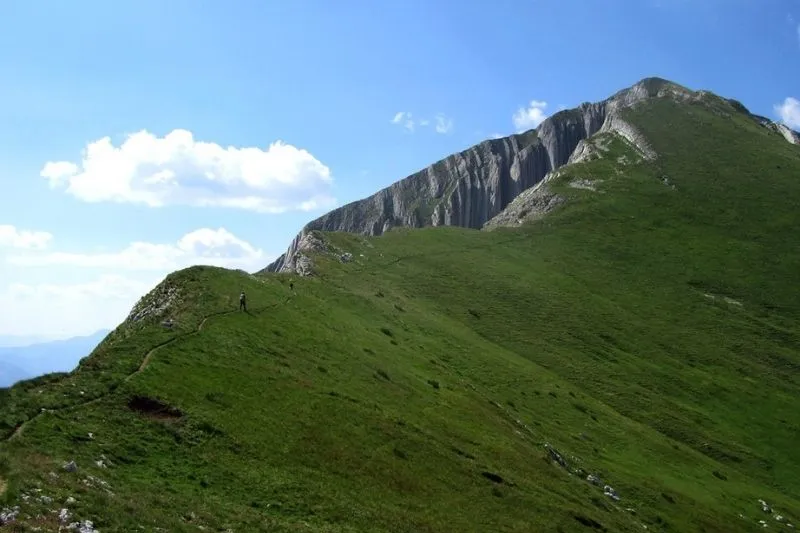 Die grüne Bergflanke mit Wanderern in der Ferne.
