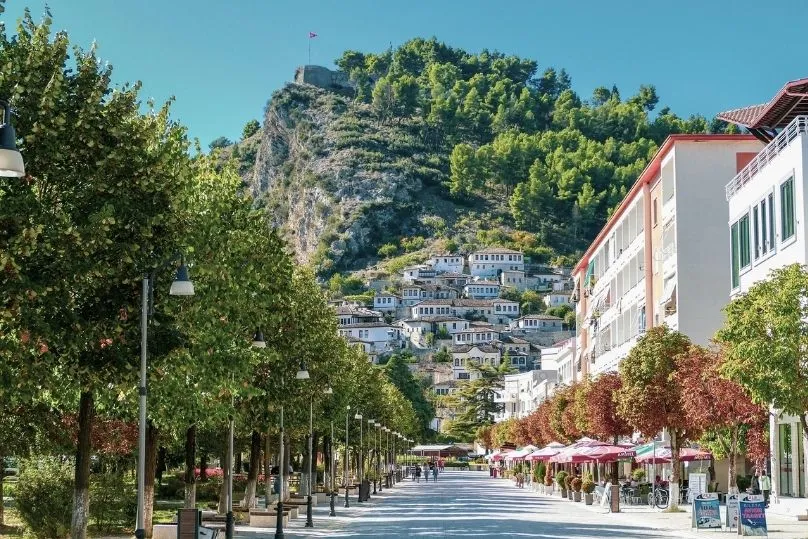 Berat mit Burgberg, weißen Häusern und lebendiger Promenade im Vordergrund.
