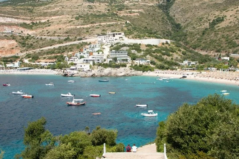 Die Bucht von Himara mit türkisblauem Wasser, kleinen Booten und entspannter Strandstimmung.