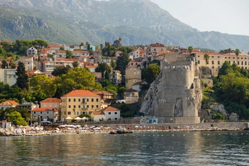 Herceg Novi mit historischen Gebäuden, Strandpromenade und Bergkulisse.