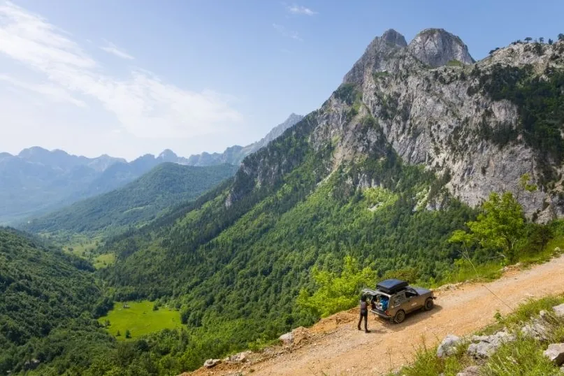 Person bei seinem Auto auf einer Bergstraße.