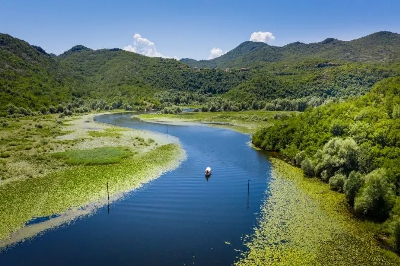 Der malerische Skutarisee mit einem sich schlängelnden Fluss, umgeben von grünen Hügeln und Seerosenfeldern.