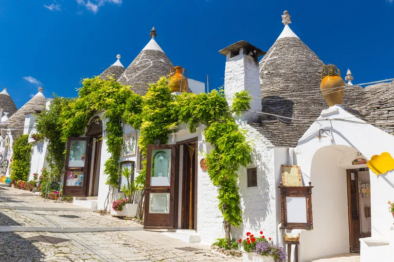 Wunderschöne Stadt Alberobello mit ihren Trulli Häusern zwischen grünen Pflanzen und Blumen im historischen Zentrum, Region Apulien, Süditalien