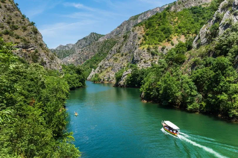 Ein Boot fährt durch eine Schlucht mit türkisem Wasser in Nordmazedonien im Nationalpark Matka.