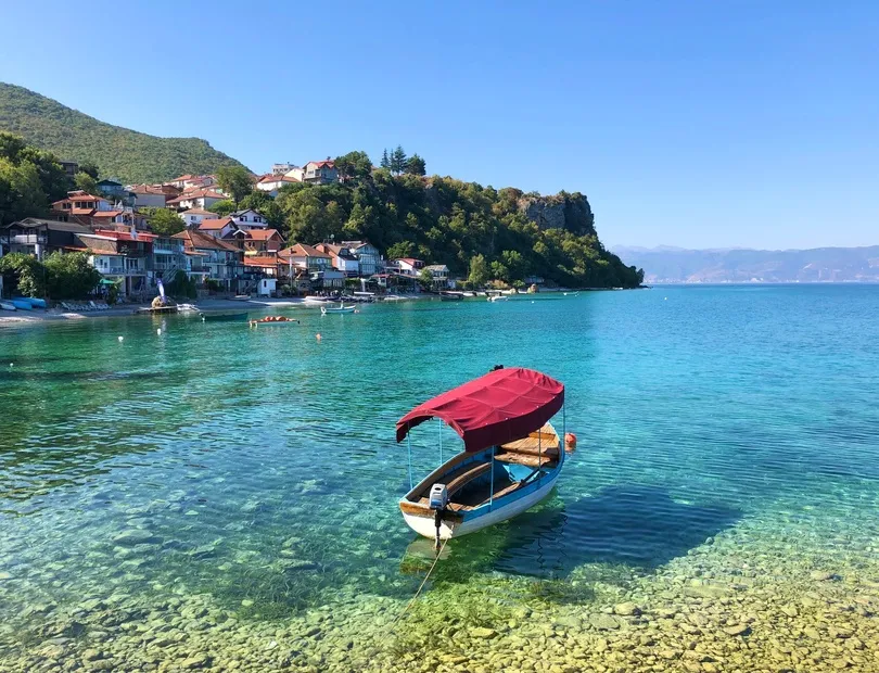 Ein einzelnes Fischerboot treibt im türkisen Wasser. Das Trpejca Fischerdorf ist im Hintergrund sichtbar.
