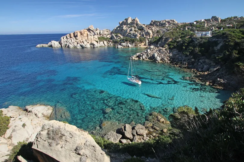  Ein Segelboot in einer versteckten Bucht auf Sardinien mit türkisem Wasser.