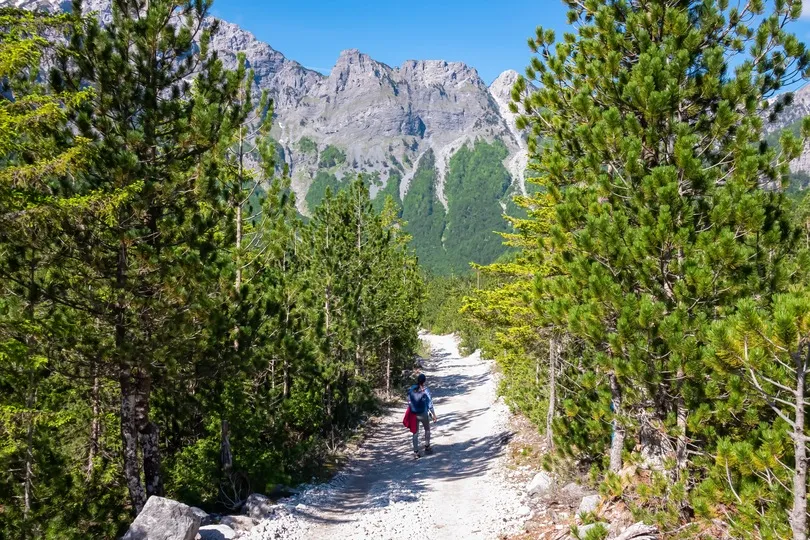 Wanderin auf dem Wanderweg von Valbona nach Theth. Im Hintergrund ragen die schneebedeckten Gipfel des Zhaborret Massivs in den Albanischen Alpen im Nationalpark Val.