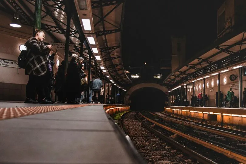 Menschen warten auf einem beleuchteten Bahnsteig in einer U-Bahn- oder Bahnstation bei Nacht.