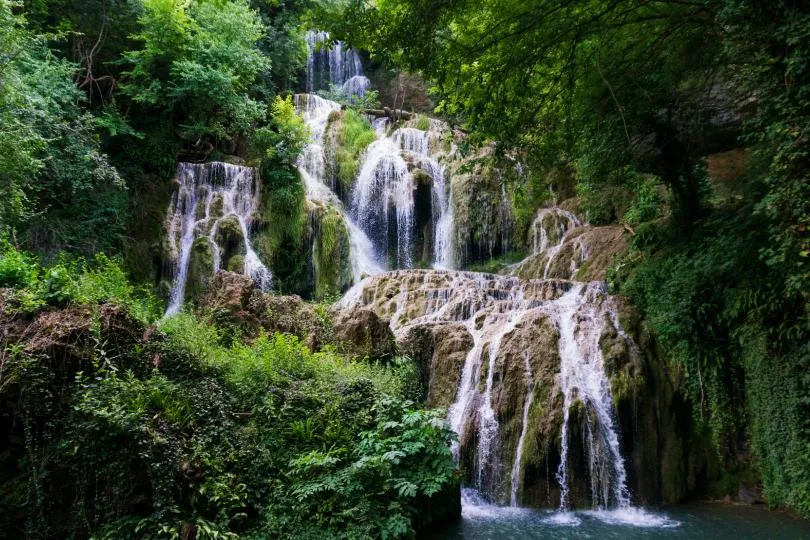 Krushuna-Wasserfälle in Bulgarien mit mehreren Kaskaden über moosbewachsene Felsen im grünen Wald.