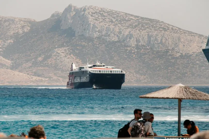 Fähre in Griechenland. Im vordergrund Touristen an einer Strandbar.
