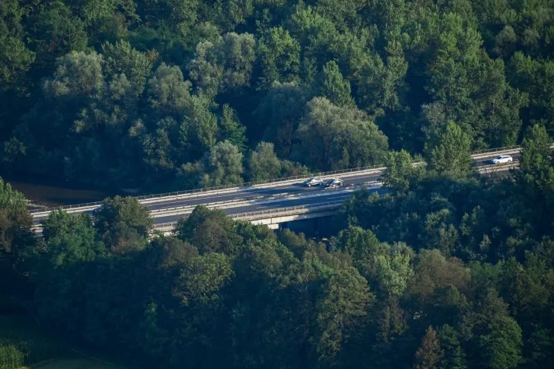 Autobahnbrücke mit fahrenden Autos, die durch eine dicht bewaldete Landschaft führt, aus der Vogelperspektive aufgenommen.