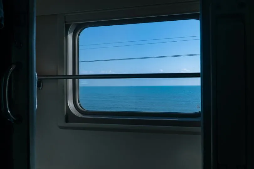 Blick aufs blaue Meer aus einem fahrenden Zug.