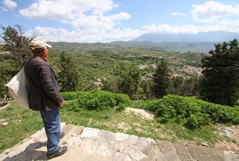 Mann in Albanien schaut hinab auf ein Dorf im Grünen.