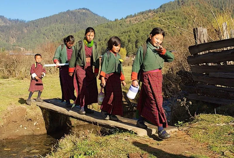 Kinder überqueren eine Holzbrücke in Bhutan.