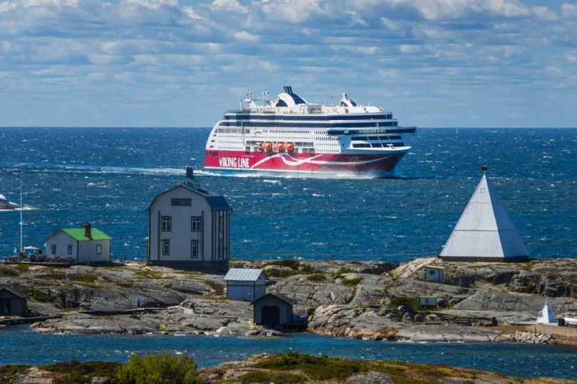 Viking-Line-Fähre auf der Ostsee zwischen Schweden und Finnland, davor Schärenfelsen mit Häusern und Leuchtturm.