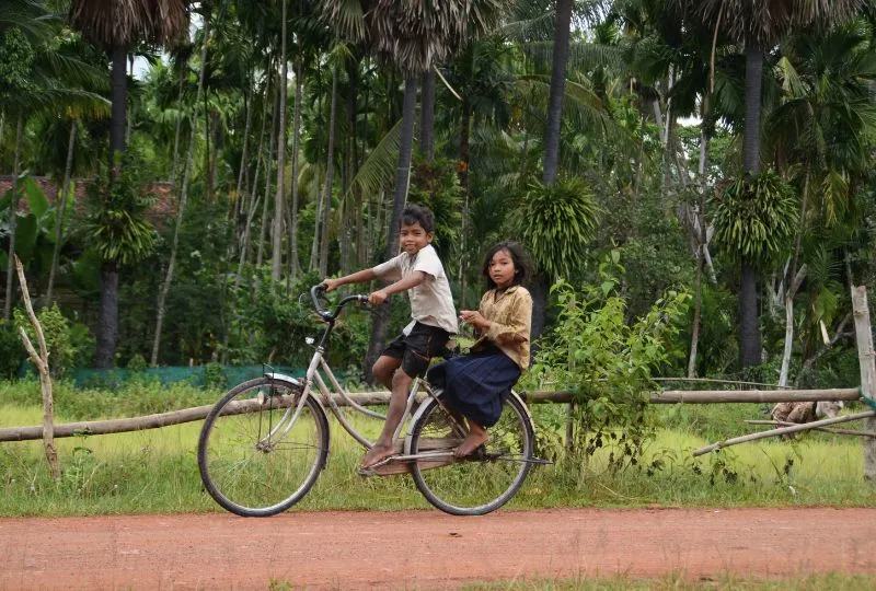 Zwei Kinder fahren auf einem Fahrrad durch Kambodschas Land.