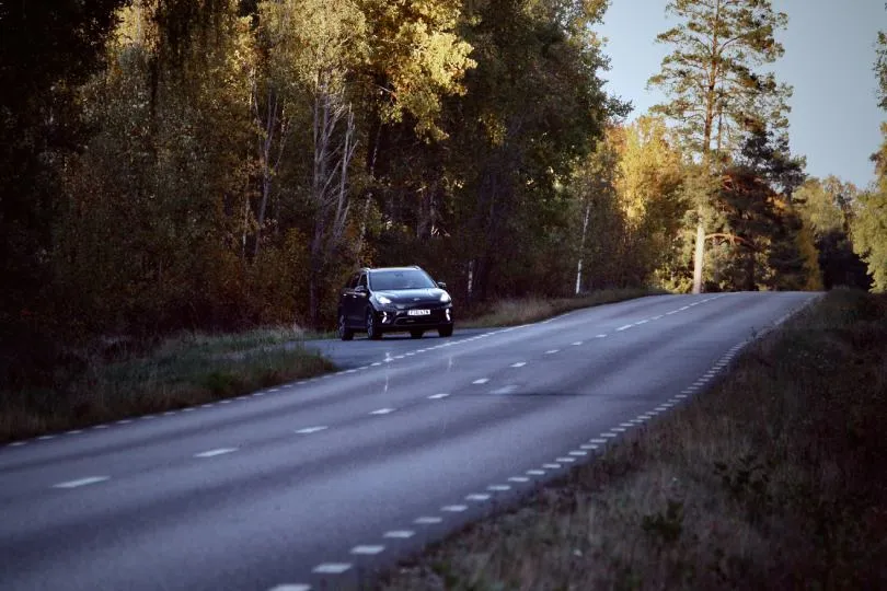 Auto fährt auf einer Landstraße durch herbstlichen Wald in Schweden bei warmem Licht.