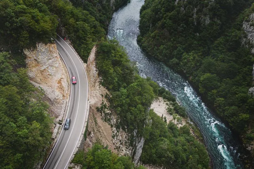 Kurvenreiche Straße verläuft entlang einer steilen Schlucht, während ein Fluss durch das Tal unterhalb fließt, aufgenommen aus der Vogelperspektive.