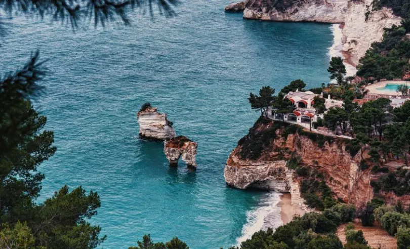 Steilküste in Apulien mit weißen Felsen, türkisfarbenem Wasser und Felsformationen im Meer.