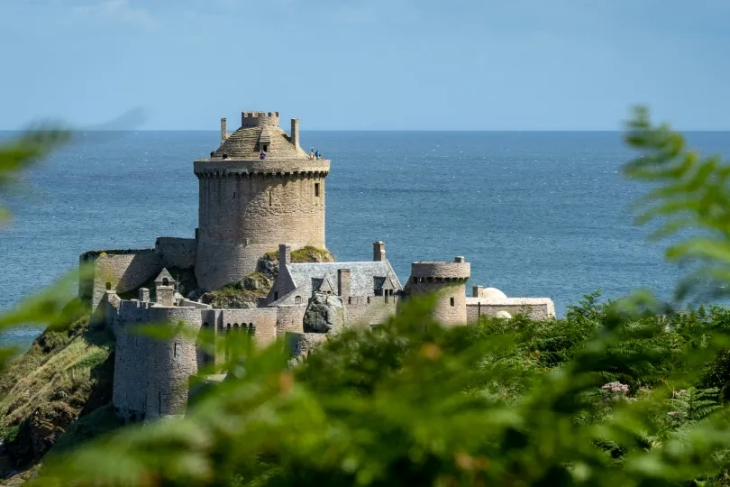Steinerne Burg an der bretonischen Küste auf einer kleinen Landzunge mit Blick auf das Meer, umgeben von grüner Vegetation.