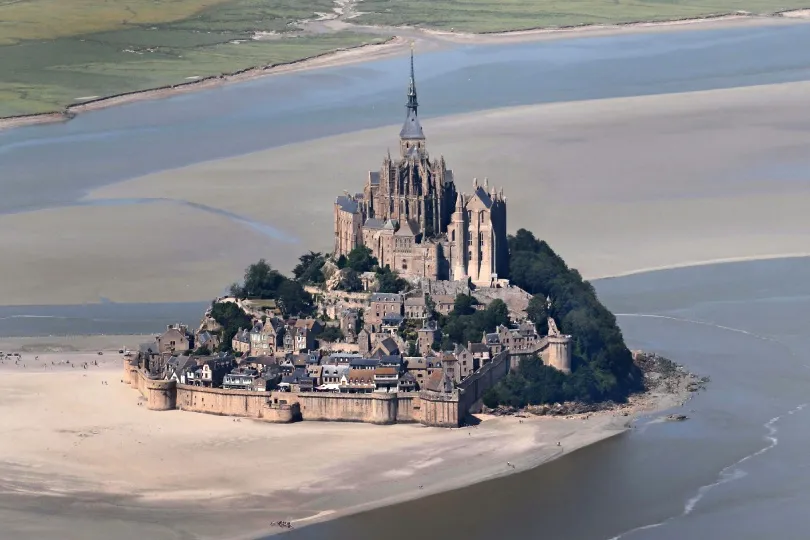 Mont-Saint-Michel in der Normandie, eine mittelalterliche Abtei auf einer felsigen Insel, umgeben von weiten Sandflächen bei Ebbe.
